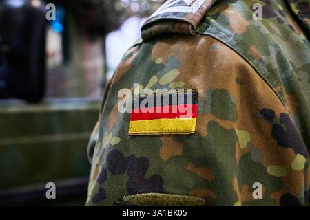 Augsburg, Bayern, Deutschland - 7. März 2025: Ein Bundeswehrsoldat in Tarnuniform mit der deutschen Flagge als Abzeichen auf der Schulter. Die Militäruniform zeigt das klassische Tarnmuster *** ein Bundeswehrsoldat in Tarnuniform mit der deutschen Flagge als Abzeichen auf der Schulter. Die Armeeuniform zeigt das klassische Camouflage-Muster Stockfoto