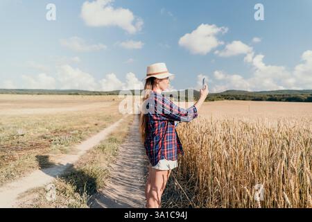 Eine junge Frau, die ein Foto von einem Weizenfeld macht Stockfoto