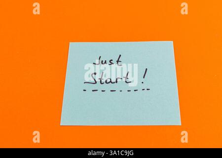 Eine einfache Notiz auf einem hellorangefarbenen Hintergrund zeigt die Worte Just Start!. Diese Motivationsbotschaft inspiriert einzelne dazu, Maßnahmen zu ergreifen und zu beginnen Stockfoto