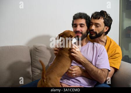 Schwule Paare spielen mit Hund auf Sofa zu Hause Stockfoto