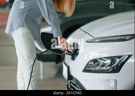 Anschließen des Ladegeräts. Nahaufnahme einer Frau mit Elektroauto. Stockfoto