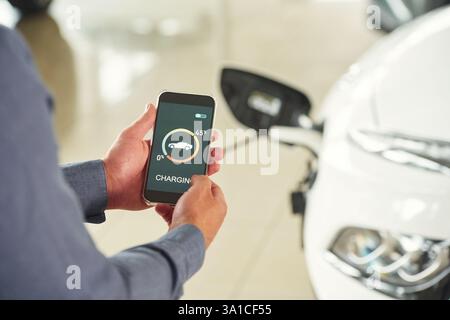 Ladevorgang über die Smartphone-App. Nahaufnahme eines Mannes mit Elektroauto. Stockfoto