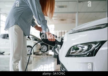 Anschließen des Ladegeräts. Nahaufnahme einer Frau mit Elektroauto. Stockfoto