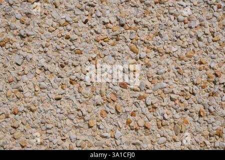 Eine Wand mit einer weißen und braunen Steinoberfläche. Der Stein besteht aus kleinen Felsen und Kieselsteinen Stockfoto