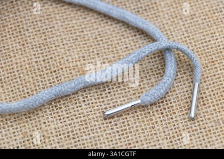 Hellgrauer Schnürsenkel mit silbernem Metallstift auf Sackleinen Hintergrund, Nahaufnahme, Makrofotografie. Stockfoto