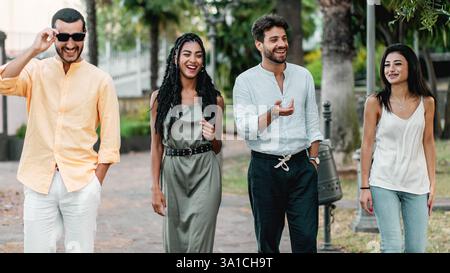 Eine Gruppe junger, vielfältiger Freunde spazieren und lachen gemeinsam in einem urbanen Park und genießen einen ungezwungenen und entspannten Outdoor-Moment. Stockfoto