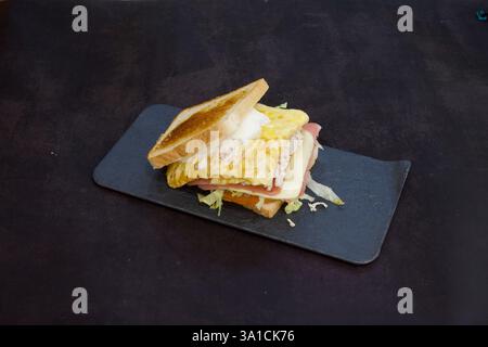 Ein Sandwich mit Schinken und Käse auf einem schwarzen Teller. Das Sandwich ist geröstet und hat einen Aufstrich Mayonnaise Stockfoto