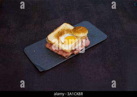 Ein Sandwich mit einem Spiegelei drauf. Das Sandwich ist auf einem schwarzen Teller. Das Ei ist leicht verbrannt Stockfoto