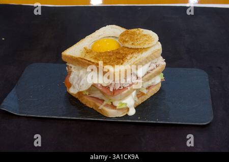 Ein Sandwich mit einem Spiegelei drauf. Das Sandwich besteht aus zwei Brotstücken mit einer Schicht Schinken und Salat dazwischen Stockfoto