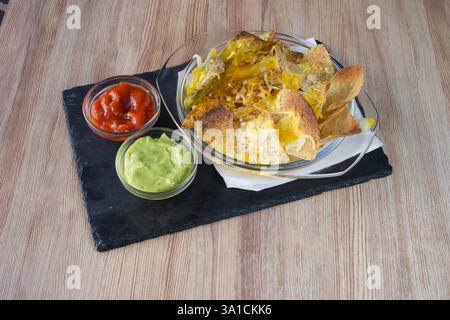 Ein Teller Nachos mit Guacamole und Salsa. Der Tisch ist aus Holz und das Geschirr aus Glas Stockfoto
