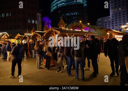 Eine große Gruppe von Menschen versammelt sich auf dem Weihnachtsmarkt am Potsdamer Platz, um an diesem Winterabend warme Speisen und Glühwein zu genießen Stockfoto