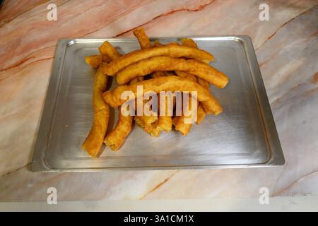Ein Tablett mit gebratenen Donuts steht auf einer Marmorarbeitsfläche. Die Donuts sind goldbraun und scheinen frisch zubereitet zu sein. Das Tablett ist silberfarben und hat eine rechteckige Stockfoto