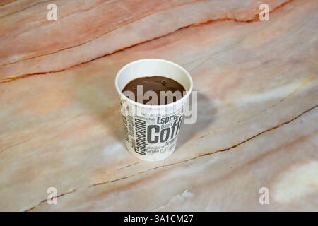 Eine Tasse Kaffee steht auf einer Marmorplatte. Die Tasse ist weiß und hat ein Design von Kaffeebohnen. Der Kaffee ist heiß und kann man genießen Stockfoto