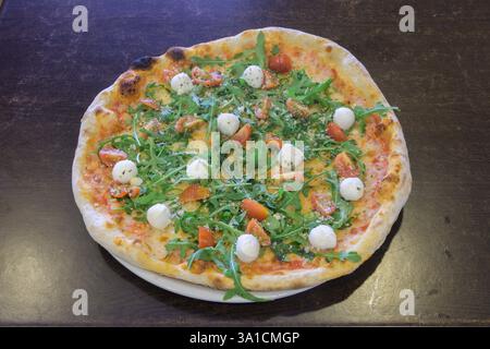 Eine Pizza mit Spinat und Käse drauf. Die Pizza steht auf einem Holztisch. Die Pizza ist sehr groß und hat viele Beläge Stockfoto