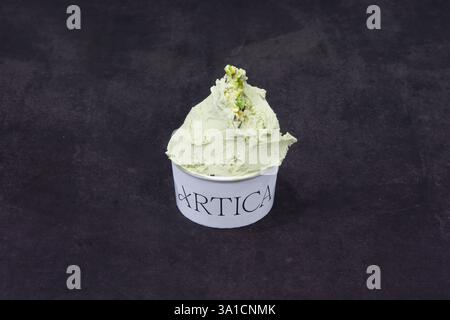 Eine Schaufel grünes Eis in einer weißen Tasse mit dem Wort Artica darauf. Das Eis sitzt auf einer schwarzen Oberfläche Stockfoto