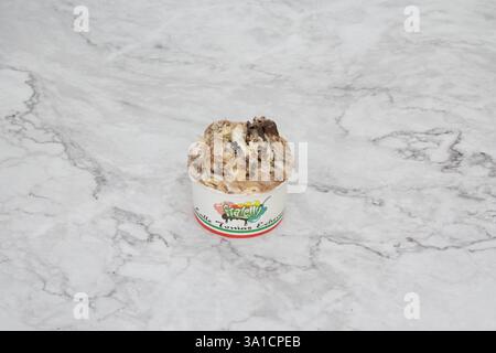 Eine kleine Eiskugel mit einem weißen Kegel und einem grünen und roten Etikett. Der Tiegel ist mit Eis gefüllt und hat einen Schokoladenbelag Stockfoto