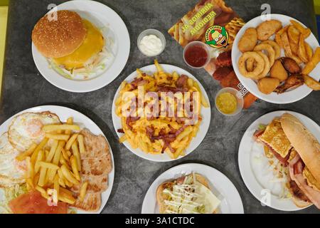Ein Tisch mit verschiedenen Speisen, darunter Sandwiches, Pommes Frites und Hähnchenflügel. Der Tisch ist für eine Mahlzeit gedeckt und das Essen sieht köstlich aus Stockfoto