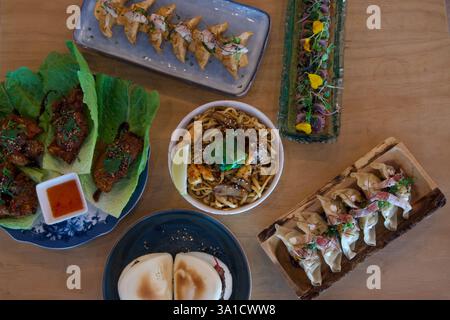 Ein Tisch ist mit einer Vielzahl asiatischer Gerichte gefüllt, darunter Knödel, Nudeln und Pfannkuchen. Es gibt mehrere Schüsseln und Teller mit Speisen, jede mit Di Stockfoto