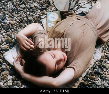 Eine junge Frau, die am Strand in Brighton liegt, mit geschlossenen Augen, mit zwei Büchern an der Seite von ihr, einer davon ist die Dark Street von Peter Cheyney, 1939. Aus „Time to Remember – The Reluctant Warriors“, 1939 (Reel 1); Dokumentarfilm über Ereignisse von 1939 – Vorbereitungen für den Krieg und dann Feindseligkeiten brechen aus. (Farbige Schwarz-weiß-Standbilder) Stockfoto