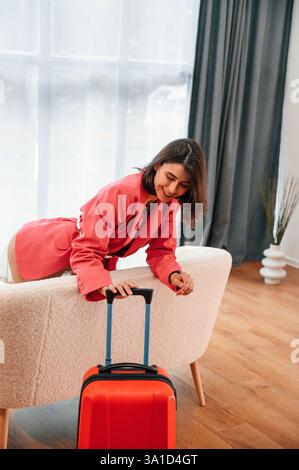 Schaut sich den Koffer an. Frau in roter Kleidung ist drinnen im Wohnzimmer. Stockfoto