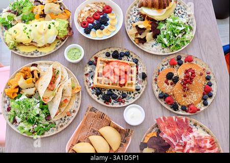 Ein Tisch voller Speisen mit einer Auswahl an Gerichten einschließlich Waffeln, Pfannkuchen und Sandwiches. Der Tisch ist für eine Mahlzeit gedeckt und das Essen sieht köstlich aus Stockfoto