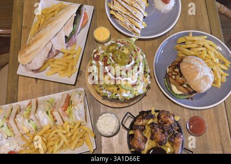 Ein Tisch mit verschiedenen Speisen, darunter Sandwiches, Hähnchenflügel und Pommes frites. Die Szene ist zwanglos und einladend, da es sich um ein Buffet-Menü handelt Stockfoto