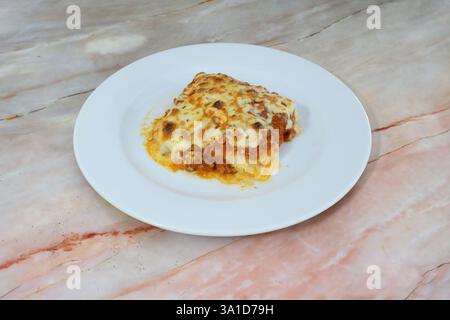 Ein Teller Lasagne steht auf einer Marmorarbeitsfläche. Das Gericht ist mit Käse- und Fleischsoße bedeckt und sieht köstlich aus Stockfoto