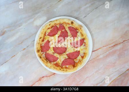 Eine Pizza mit Peperoni-Scheiben auf einem weißen Teller. Die Pizza steht auf einer Marmorplatte Stockfoto