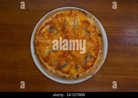 Eine Pizza mit viel Käse und Tomatensauce sitzt auf einem Holztisch. Die Pizza ist groß und hat viele Beläge, so dass sie sehr appetitlich aussieht Stockfoto