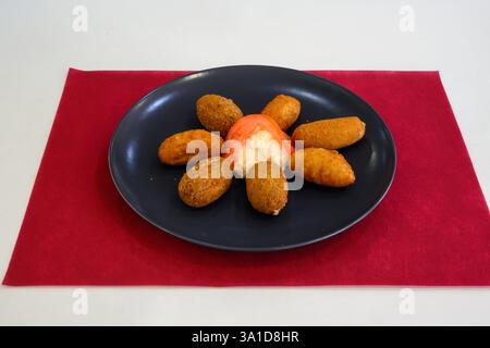 Ein Teller mit frittiertem Essen mit einem roten Tuch darunter. Der Teller ist voller verschiedener Arten von Speisen, einschließlich gebratener Donuts und einer cremigen Sauce Stockfoto