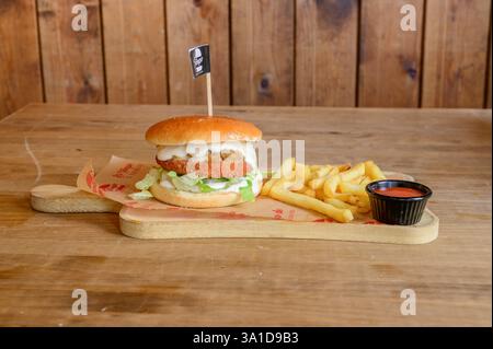Ein Burger mit einer Flagge und einer Seite Pommes. Der Burger ist auf einem Holzbrett und die Pommes sind in einem schwarzen Behälter Stockfoto