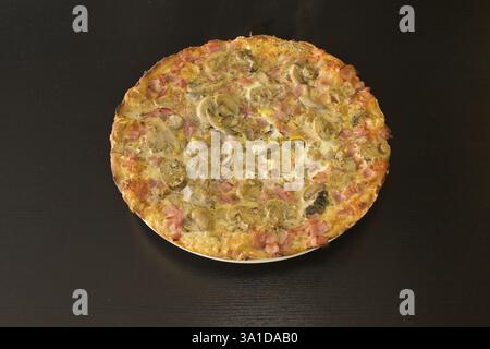 Eine Pizza mit Pilzen und Schinken drauf. Die Pizza steht auf einem schwarzen Tisch. Die Pizza ist sehr groß und hat viele Beläge Stockfoto