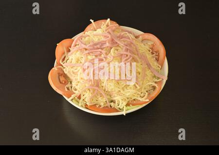 Ein Teller mit viel Käse und Tomaten. Die Platte steht auf einem schwarzen Tisch Stockfoto