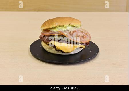Ein Hamburger mit Käse und Tomaten auf einem schwarzen Teller. Der Hamburger ist groß und hat viele Beläge Stockfoto