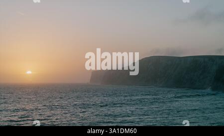 Die Sonne untergeht über dem Meer und strahlt ein warmes Leuchten über das Wasser und die felsigen Klippen Stockfoto