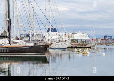 Valencia, Spanien - 23. Februar 2025: Ruhige Yachtszene mit mehreren Yachten und kleineren Booten, die in ruhigen Gewässern angedockt werden. Eine große Fähre ist sichtbar. Stockfoto