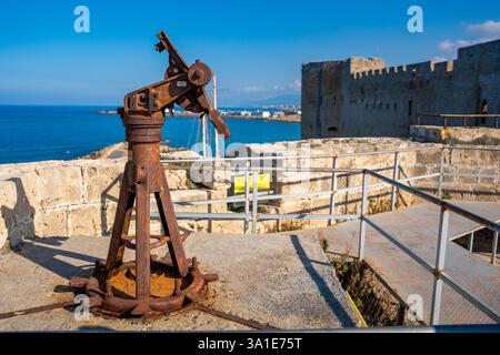 Alter Artilleriemechanismus auf den Festungsmauern von Kyrenia in Nordzypern. Das alte militärische Relikt steht vor dem Hintergrund des Meeres und Stockfoto