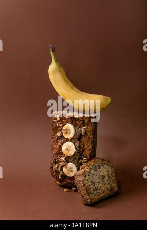 Modernes Stillleben mit hausgemachtem Bananenbrot. Brot mit Walnüssen, bestreichen Karamell, belegt mit frischer Banane auf braunem Hintergrund. Levitation Banane abo Stockfoto