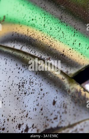 Veralteter Spiegel mit Rissen und beschädigten Stellen, an denen die reflektierende Rückseite verschwunden ist, verzerrt Formen in Grün- und Gelbtönen Stockfoto