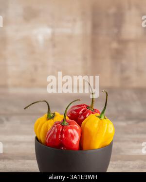 Gelbe und rote Habanero-Paprika in schwarzer Schüssel auf hölzernem Hintergrund Stockfoto