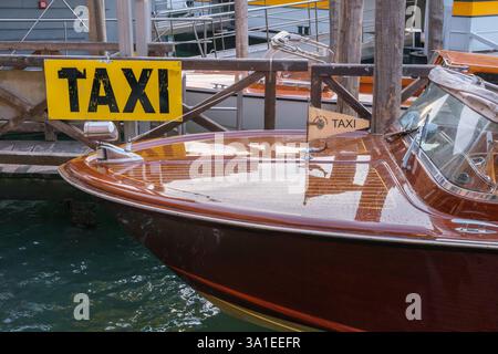 Venedig, Italien - 12. Oktober 2024: Ein klassisches hölzernes Wassertaxi legt an einem Pier mit gelbem Taxischild an Stockfoto