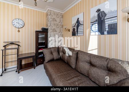 Ein Wohnzimmer mit einer großen Couch und zwei Bildern an der Wand. Die Couch ist mit gemustertem Stoff bedeckt und die Vorhänge sind weiß. Das Zimmer verfügt über eine Stockfoto