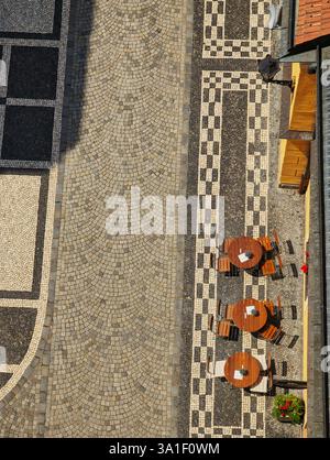 Blick aus der Vogelperspektive auf ein Café im Freien mit Holztischen und -Stühlen auf einem gemusterten Pflastersteinpflaster. Stockfoto