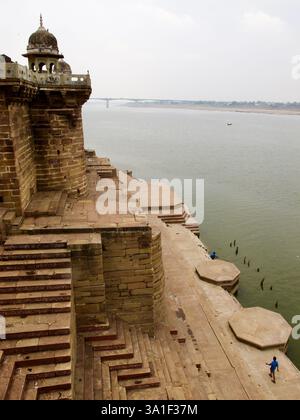 Erhöhter Blick auf den Ganges-Fluss vom Ramnagar Fort in Varanasi, mit breiten Steintreppen und der entfernten Brücke über den Fluss. Stockfoto