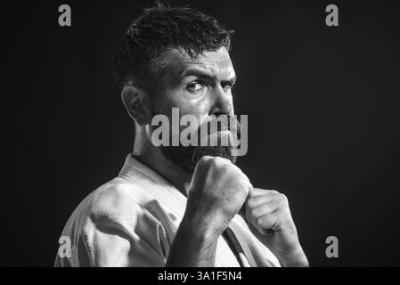 Karate-Mann. Nahaufnahme des Karatelehrers im Kimono. Ernsthafter bärtiger Karatekämpfer, der sich auf den Wettkampf im Fitnessstudio vorbereitet. Gutaussehender bärtiger männlicher Ka Stockfoto