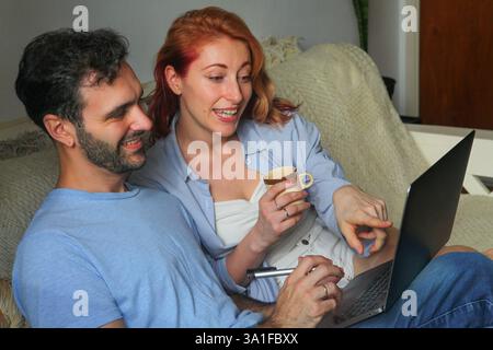 Mann und Frau, die zu Hause auf einem Laptop arbeiten, reden und lächeln Stockfoto