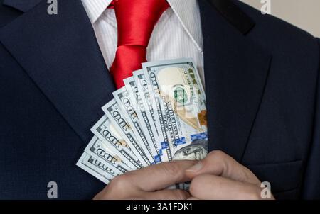 Ein reicher Mann in Anzug und Krawatte zählt US-Dollar in seiner Hand und steckt sie in seine Tasche. Geld verdienen, erfolgreicher Geschäftsmann, Investor Stockfoto