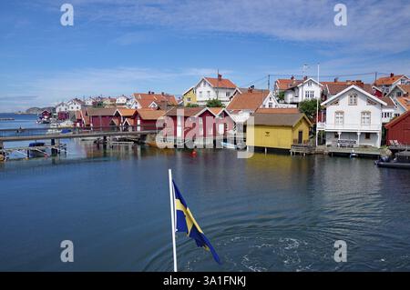 Malerisches Küstendorf mit roten und gelben Holzhäusern, schwedischer Flagge im Vordergrund, Archipel, Gullholmen, Vaestra Goetalands laen Stockfoto