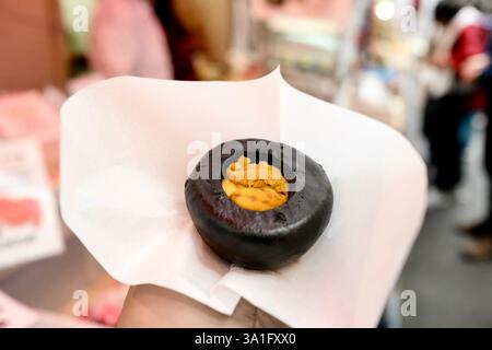 Gedämpftes Seeigel-Brötchen aus Hamada Shoten, in der Hand einer Frau auf dem Tsukiji Outer Fish Market in Chuo, Tokio, Japan Stockfoto