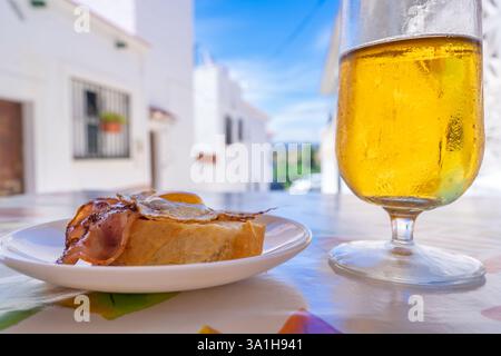 Ein Getränk mit Tapa in einem traditionellen mediterranen Dorf mit weißen Häusern an einem sonnigen Tag mit blauem Himmel. Stockfoto